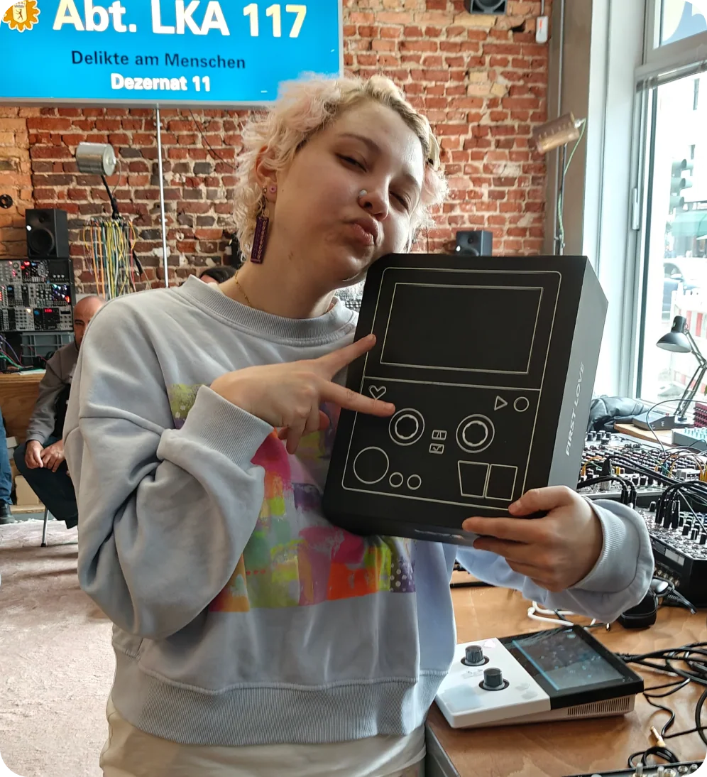 A person holding FIRST LOVE packaging in a synthesizer shop, with the instrument on the counter.