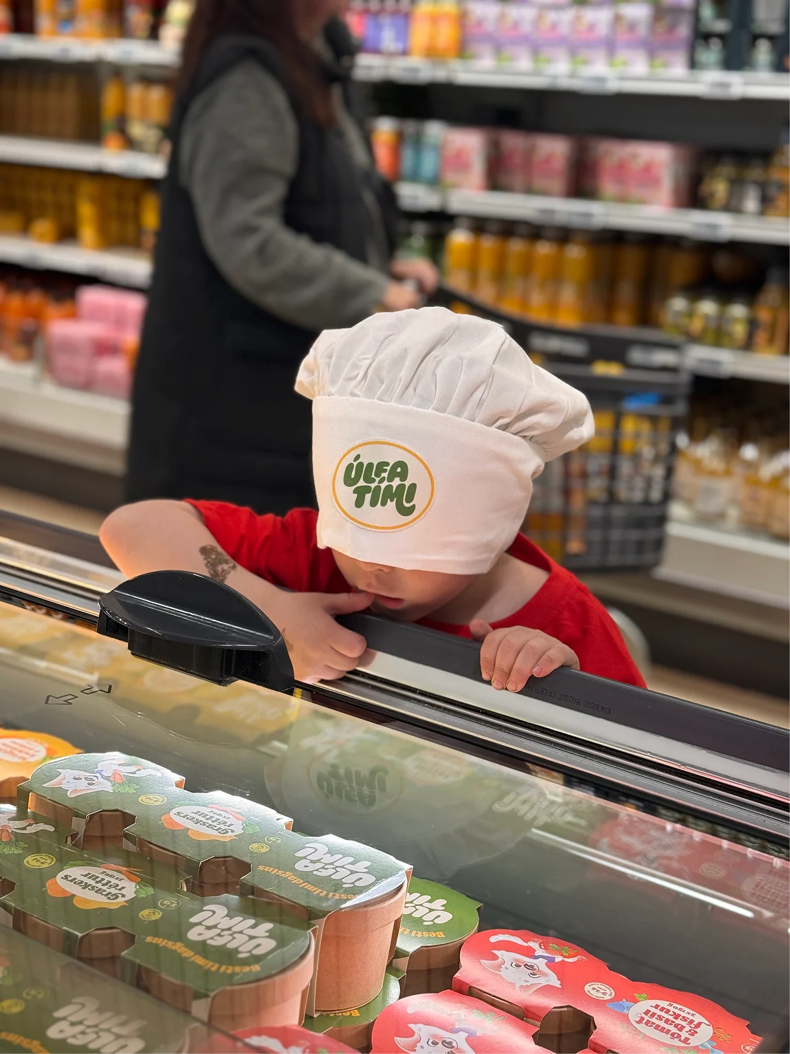 A child wearing an Úlfatími chef’s hat looking at the meals in the freezer